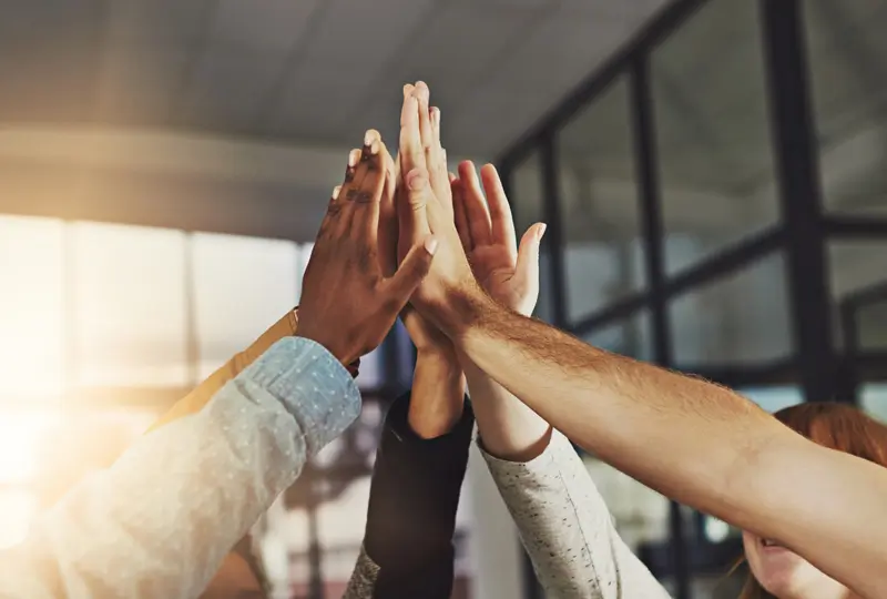 A diverse group of RTG employees high five in the middle with the sunset behind.